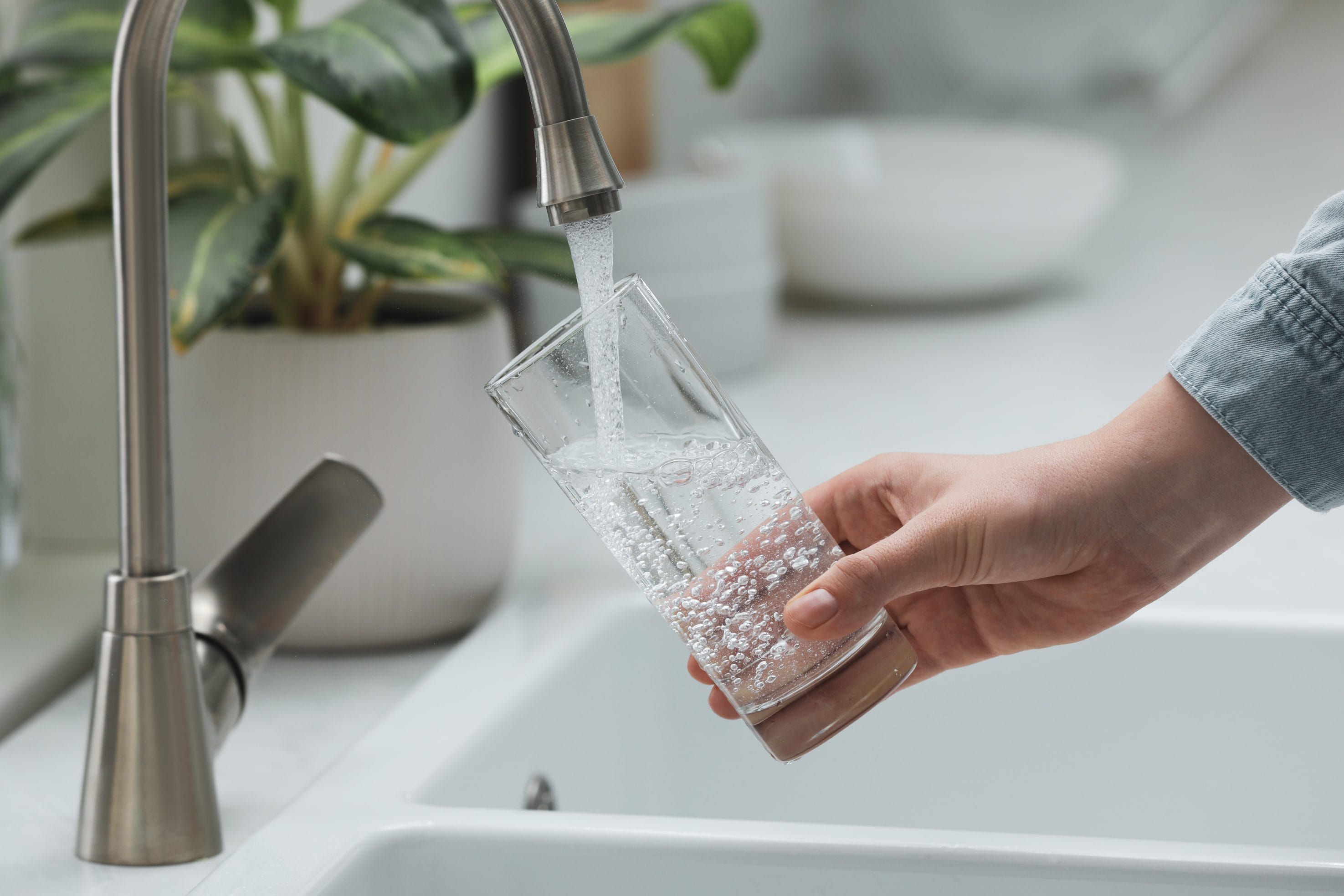 A person pours themselves a glass of water that's cleaner and clearer thanks to a water softener system.